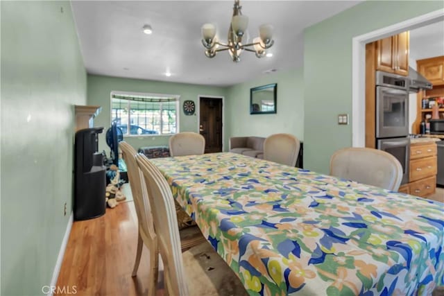 dining room featuring light wood-style floors, a notable chandelier, and baseboards