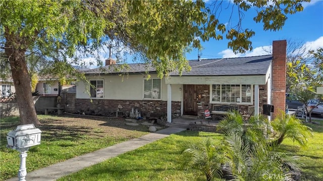 view of front of home with brick siding, stucco siding, a chimney, roof with shingles, and a front yard