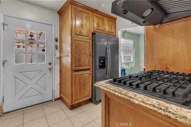 kitchen with brown cabinetry, stainless steel fridge with ice dispenser, light stone counters, black gas cooktop, and extractor fan