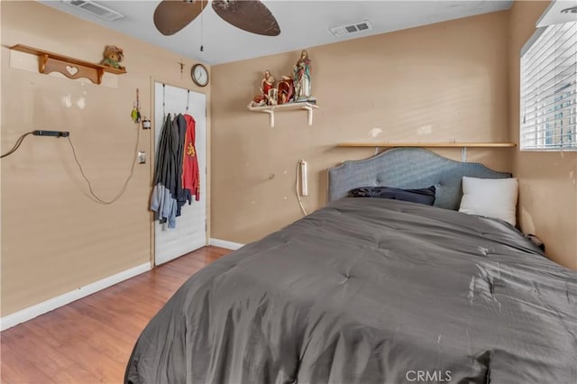 bedroom with a ceiling fan, wood finished floors, visible vents, and baseboards