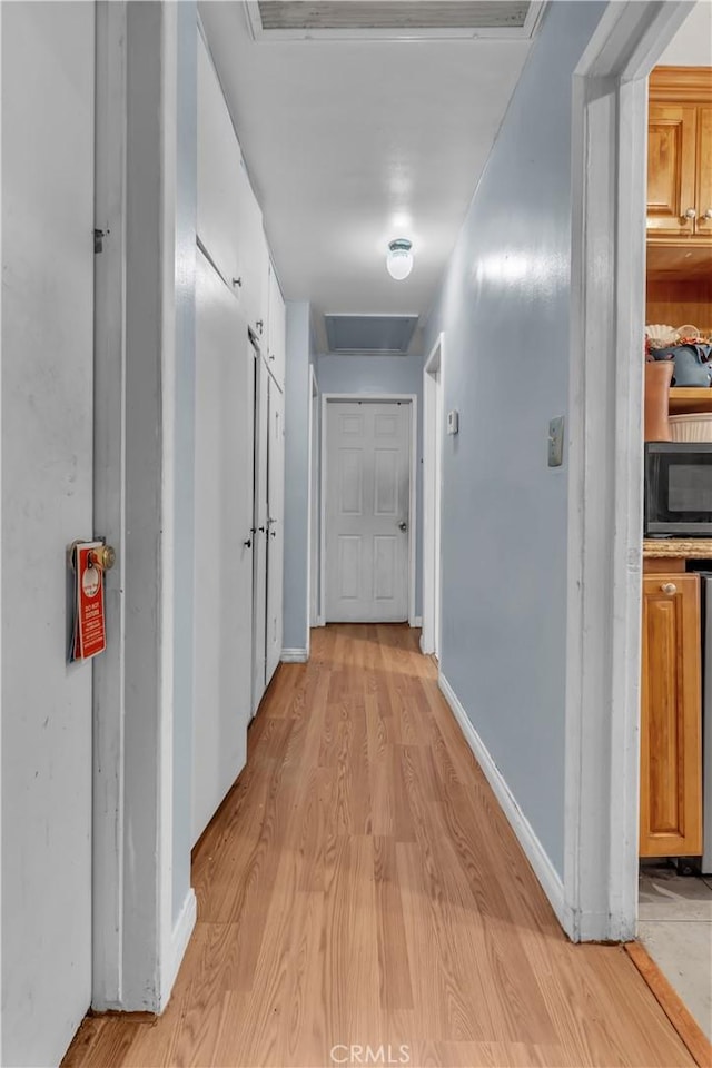 hall featuring light wood finished floors, attic access, and baseboards