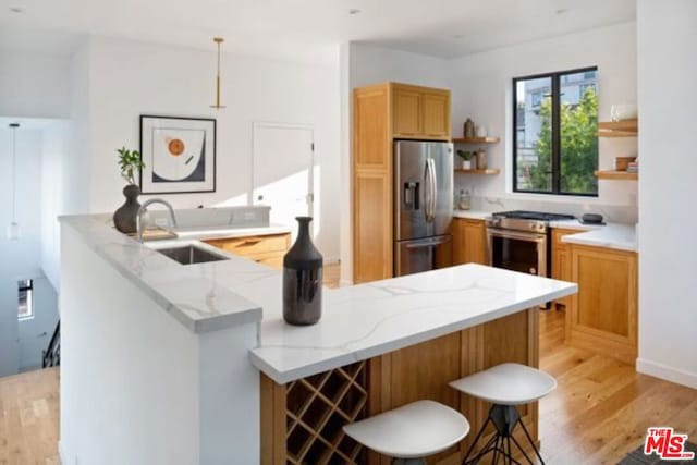 kitchen with sink, appliances with stainless steel finishes, a kitchen bar, kitchen peninsula, and light wood-type flooring