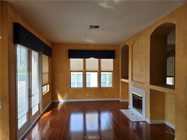 unfurnished living room with a healthy amount of sunlight, dark hardwood / wood-style flooring, and a tiled fireplace