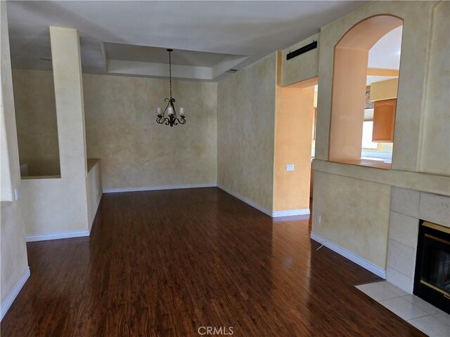 unfurnished dining area with hardwood / wood-style flooring, a tray ceiling, a tiled fireplace, and a chandelier