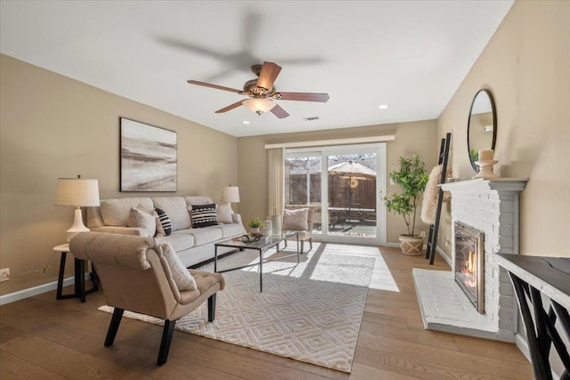 living room featuring ceiling fan, a brick fireplace, and light wood-type flooring