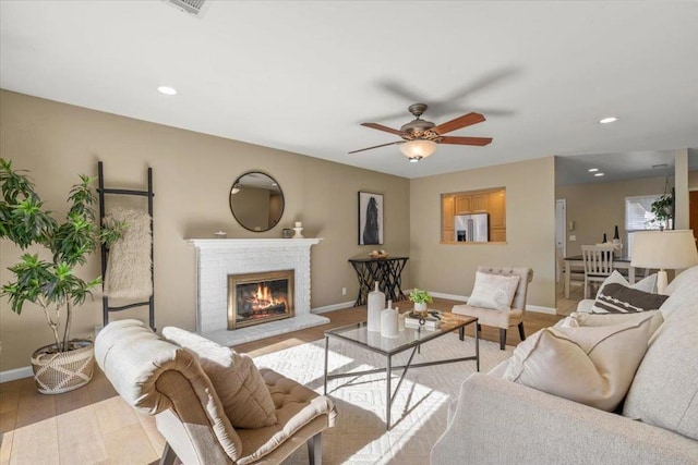 living room with ceiling fan, a brick fireplace, and light hardwood / wood-style floors