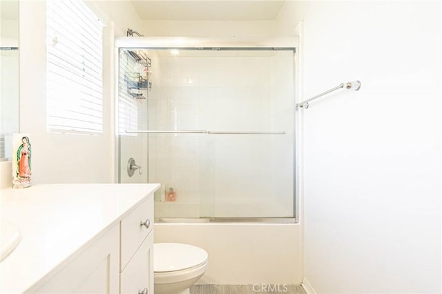 full bathroom with enclosed tub / shower combo, vanity, and toilet