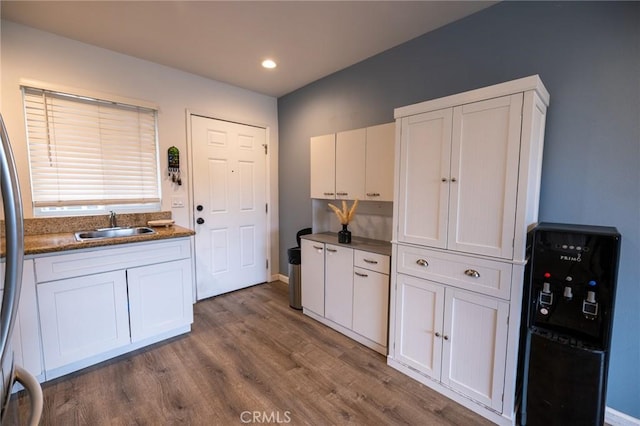 kitchen featuring sink, wood-type flooring, fridge, dark stone counters, and white cabinets