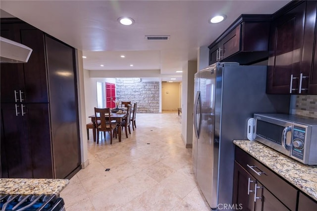 kitchen featuring dark brown cabinets, light stone countertops, and appliances with stainless steel finishes