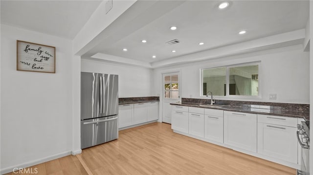 kitchen with appliances with stainless steel finishes, white cabinetry, sink, dark stone counters, and light hardwood / wood-style flooring