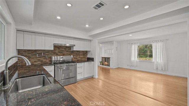 kitchen with white cabinetry, a fireplace, sink, and stainless steel gas range oven