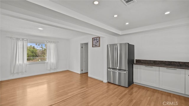 kitchen featuring stainless steel refrigerator, dark stone counters, light hardwood / wood-style flooring, and white cabinets