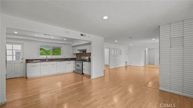 kitchen with sink, stainless steel gas range, light hardwood / wood-style flooring, white cabinetry, and backsplash