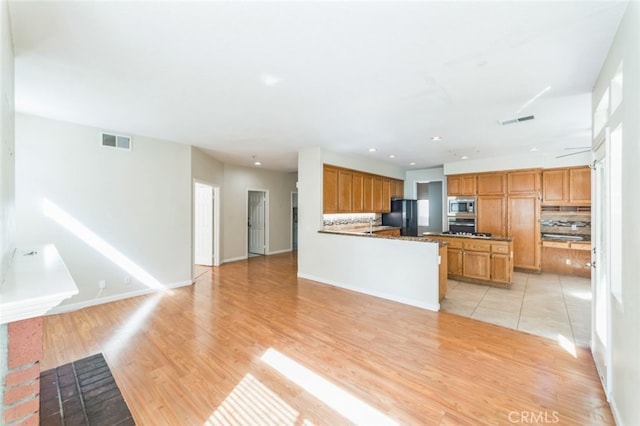 kitchen featuring tasteful backsplash, appliances with stainless steel finishes, dark stone countertops, and light hardwood / wood-style flooring