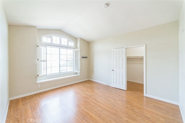 unfurnished bedroom featuring multiple windows, a walk in closet, vaulted ceiling, and light wood-type flooring