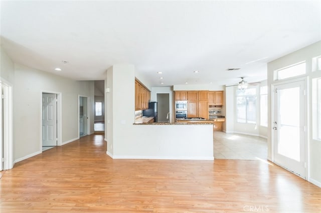 kitchen featuring light hardwood / wood-style flooring, black refrigerator, stainless steel microwave, kitchen peninsula, and stone counters