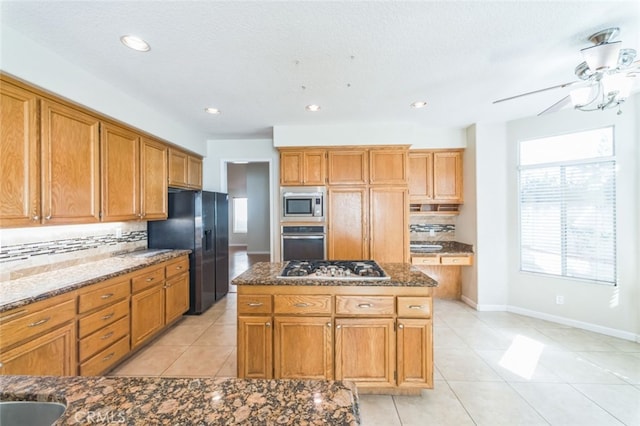 kitchen with appliances with stainless steel finishes, a center island, dark stone counters, and backsplash