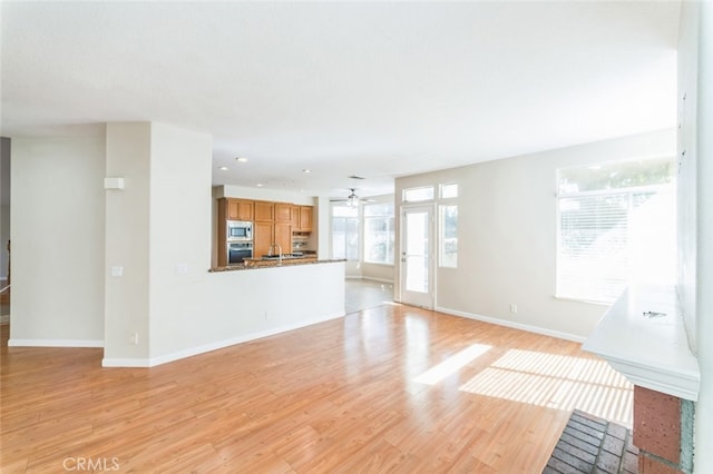 unfurnished living room featuring ceiling fan, sink, and light wood-type flooring