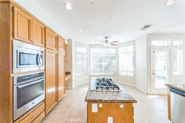 kitchen featuring a kitchen island, light tile patterned flooring, appliances with stainless steel finishes, and dark stone countertops