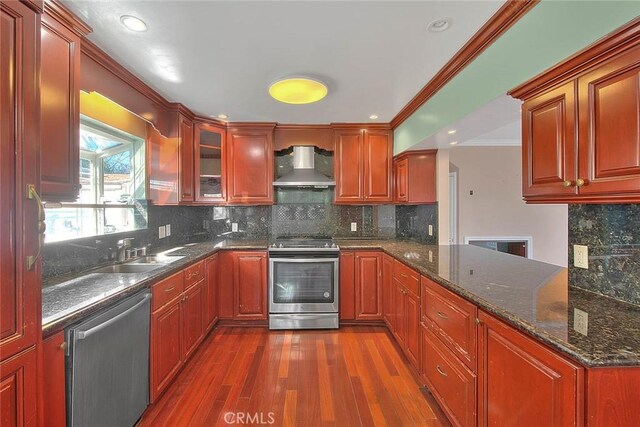 kitchen with wall chimney range hood, crown molding, dark wood-type flooring, sink, and stainless steel appliances