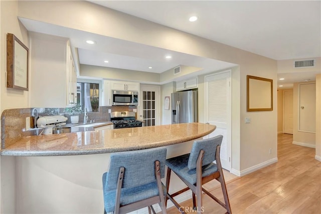 kitchen with light stone counters, light wood-style flooring, appliances with stainless steel finishes, a peninsula, and white cabinetry