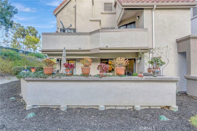 back of house with a balcony, a tiled roof, and stucco siding