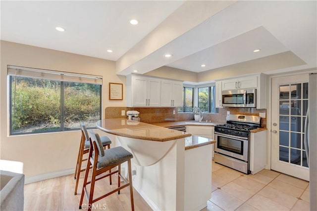 kitchen featuring a breakfast bar area, a peninsula, stainless steel appliances, white cabinetry, and backsplash