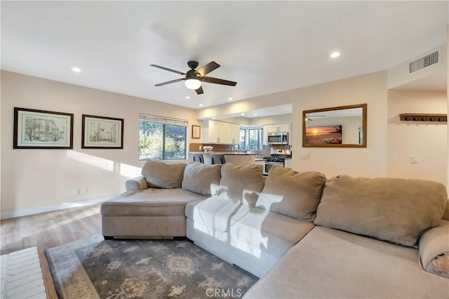 living area featuring a ceiling fan, wood finished floors, visible vents, baseboards, and recessed lighting