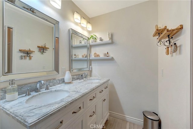 bathroom featuring double vanity, wood finished floors, baseboards, and a sink