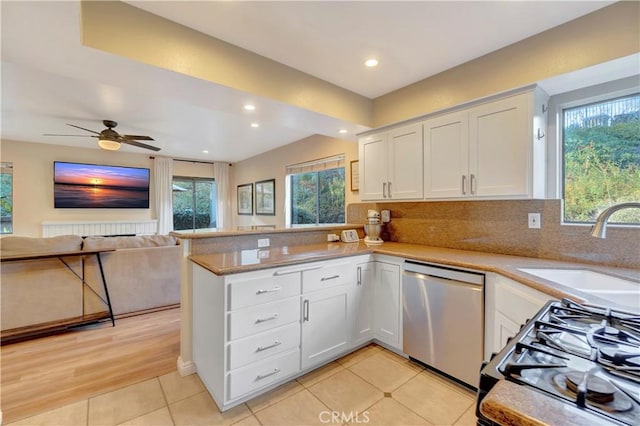 kitchen featuring a peninsula, a sink, white cabinets, stainless steel dishwasher, and tasteful backsplash