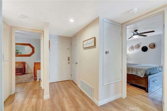 hall featuring light wood-style flooring, baseboards, and visible vents