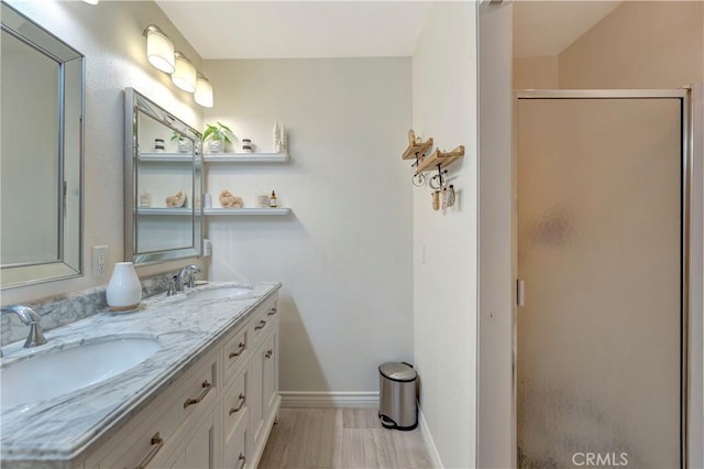 bathroom with a sink, baseboards, a stall shower, and double vanity