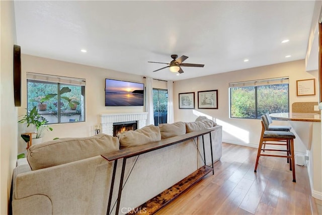 living area featuring baseboards, light wood-style flooring, recessed lighting, ceiling fan, and a brick fireplace