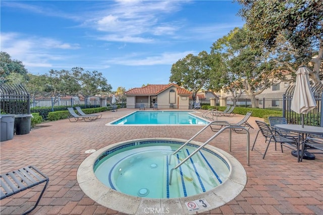 community pool with a patio area, a hot tub, and fence