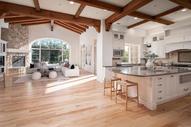 kitchen featuring stainless steel microwave, white cabinetry, a stone fireplace, and dark stone countertops