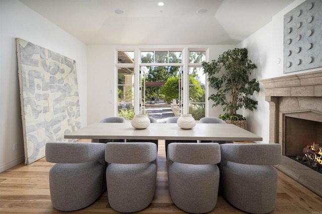 dining room featuring lofted ceiling, a stone fireplace, and light hardwood / wood-style flooring