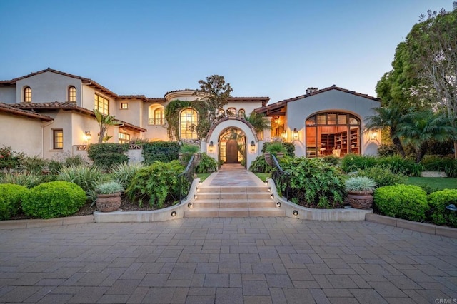 mediterranean / spanish home featuring a tile roof and stucco siding