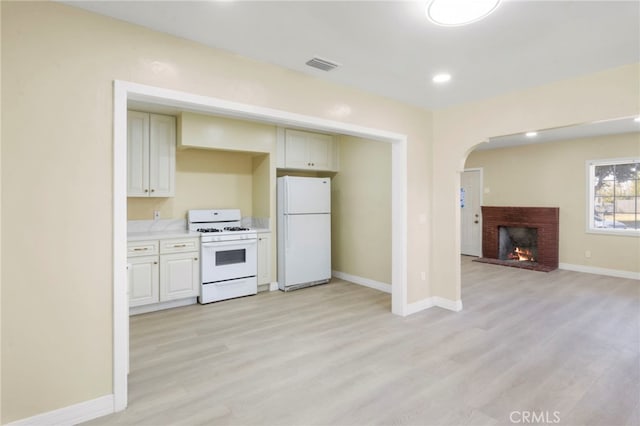 kitchen featuring white appliances, a brick fireplace, and light wood-type flooring