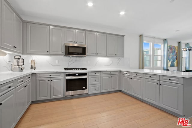 kitchen featuring appliances with stainless steel finishes, gray cabinets, light hardwood / wood-style floors, and kitchen peninsula