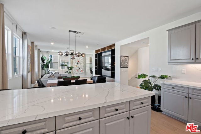 kitchen featuring gray cabinetry, decorative light fixtures, light hardwood / wood-style flooring, and light stone countertops