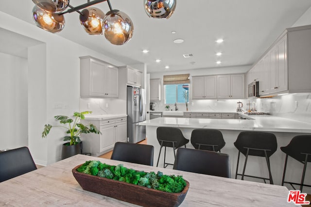 kitchen with appliances with stainless steel finishes, sink, a kitchen breakfast bar, decorative backsplash, and kitchen peninsula