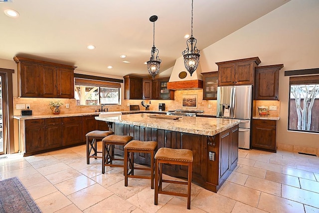 kitchen featuring a large island, lofted ceiling, light stone counters, a kitchen bar, and stainless steel fridge with ice dispenser