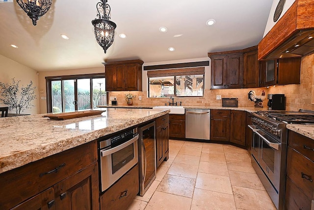 kitchen with sink, light stone counters, hanging light fixtures, stainless steel appliances, and backsplash