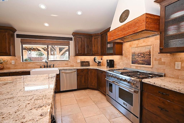 kitchen featuring sink, custom exhaust hood, light tile patterned floors, stainless steel appliances, and light stone countertops