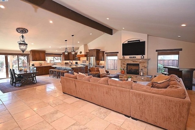 living room featuring plenty of natural light, a stone fireplace, and lofted ceiling with beams