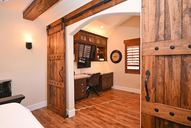 office area with vaulted ceiling with beams, dark wood-type flooring, built in desk, and a barn door