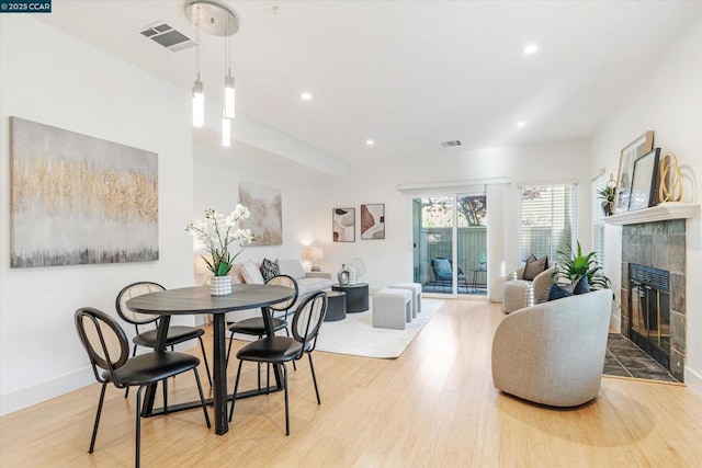 dining area with a tiled fireplace and light wood-type flooring