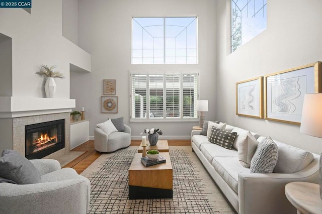 living room with a tiled fireplace, a high ceiling, and light wood-type flooring