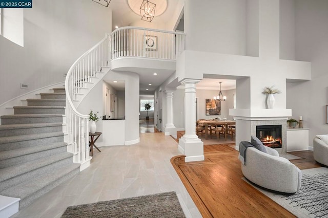 entrance foyer featuring a notable chandelier, a tiled fireplace, light wood-type flooring, and ornate columns