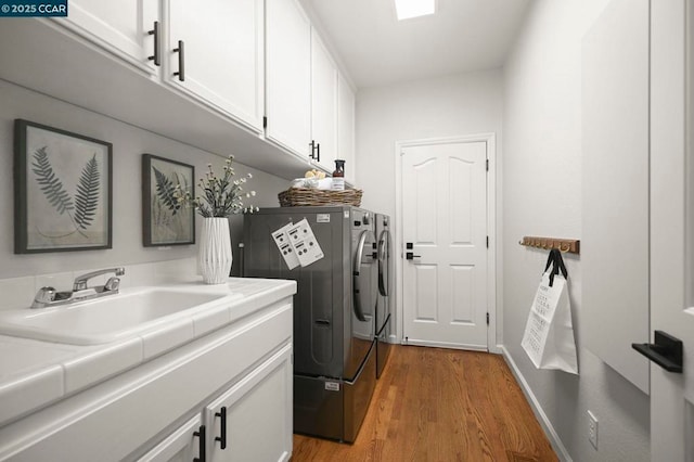 clothes washing area featuring sink, light hardwood / wood-style flooring, cabinets, and washer and dryer